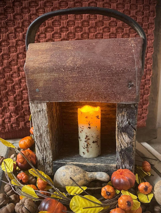 Wooden lantern with a candle, surrounded by autumn decorations on a textured surface.