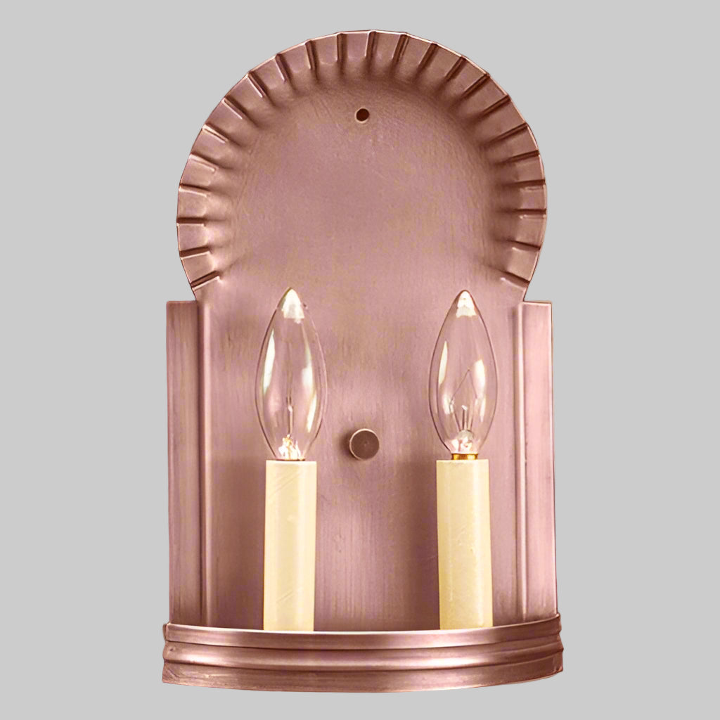 Copper wall sconce with two lit candles on a light gray background