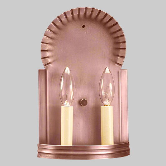 Copper wall sconce with two lit candles on a light gray background