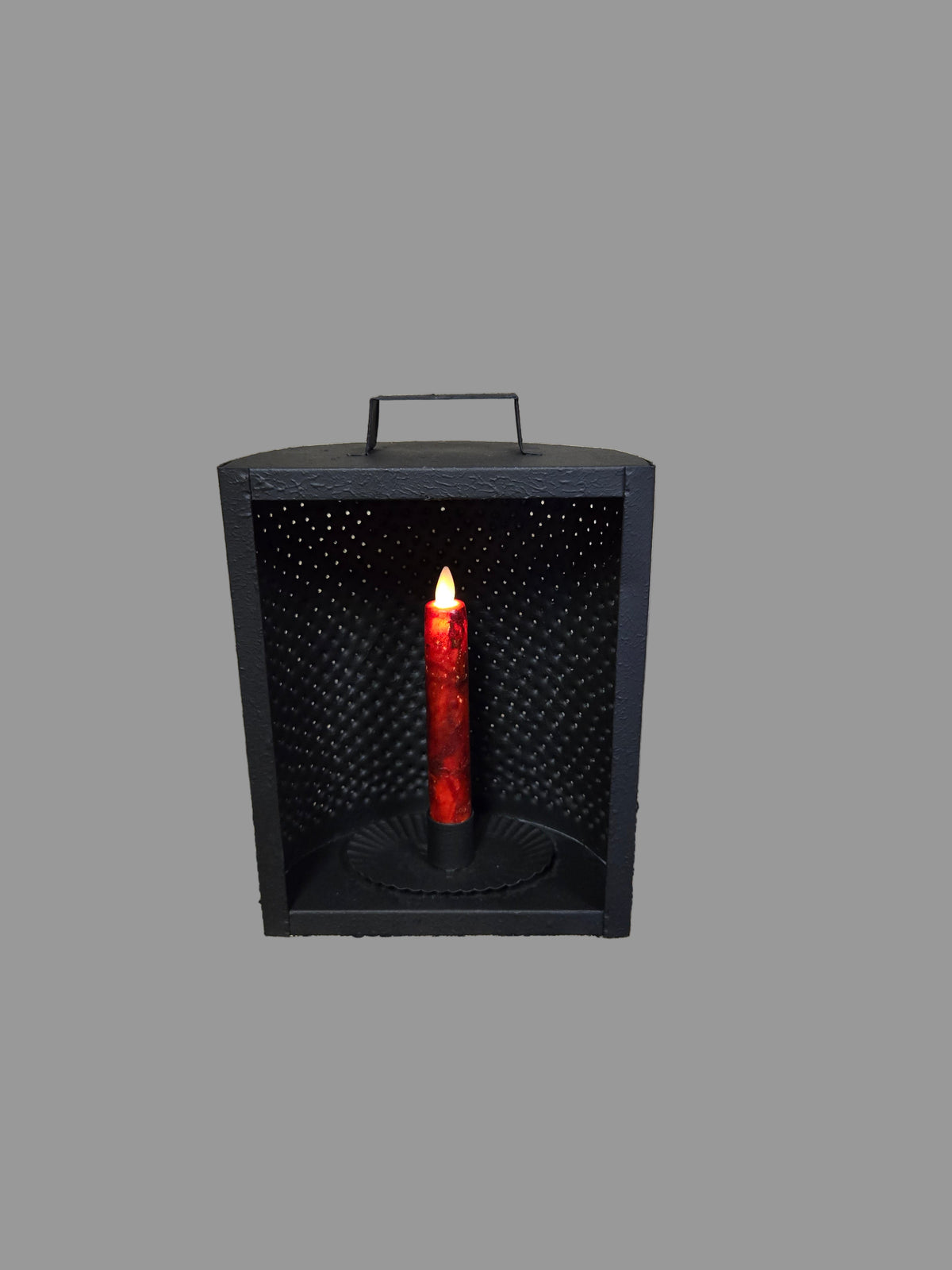 A black metal mantel light candle holder with a battery operated taper candle inside, displaying a red glow through the perforated holes.