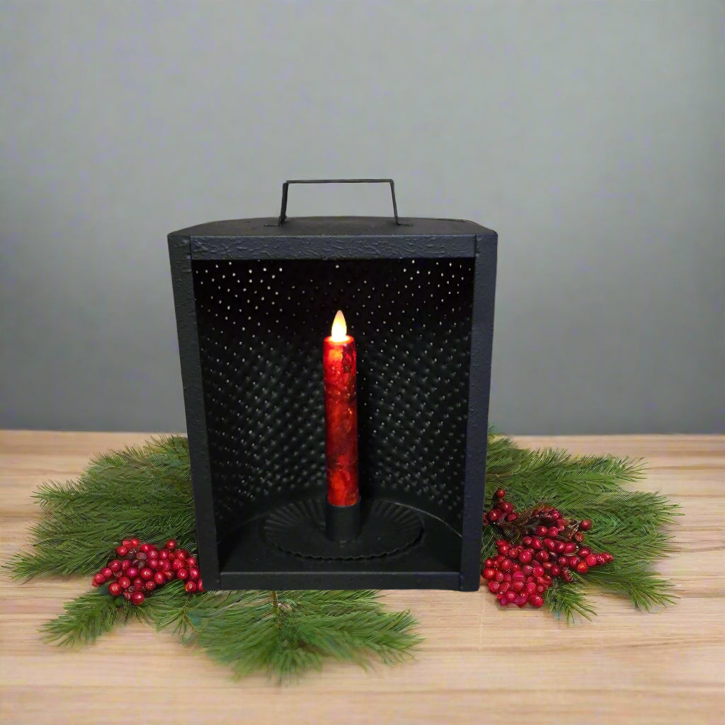 A black metal mantle light candle holder with a battery operated taper candle inside, displaying a red glow through the perforated holes.