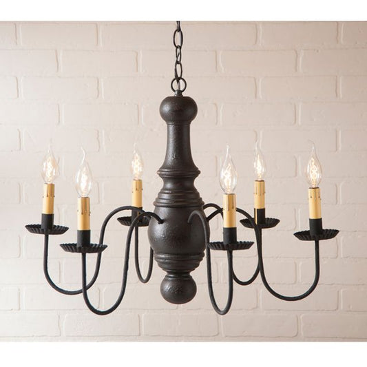 Black chandelier with six candle-style lights against a white brick wall.
