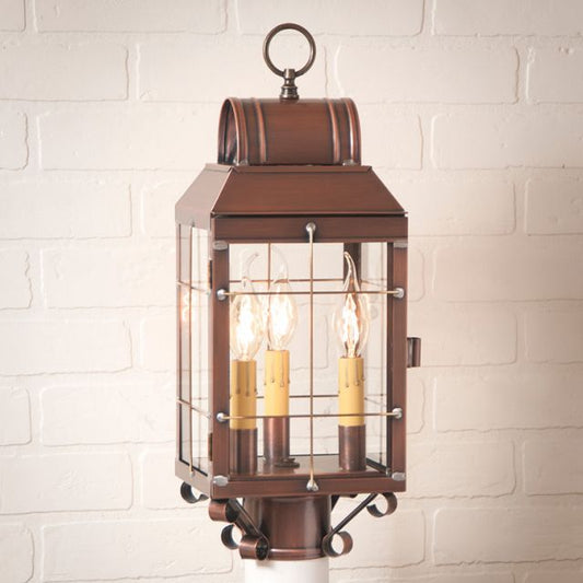 Antique copper post lantern with clear glass and three internal light bulbs, placed on a white brick column.