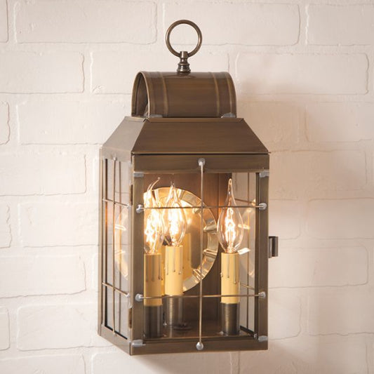 A weathered brass wall lantern with a three-light design, featuring clear glass panels and a lacquer coating.