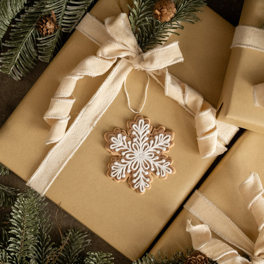 Gift wrapped in brown paper with a decorative snowflake ornament and ribbons, surrounded by greenery.
