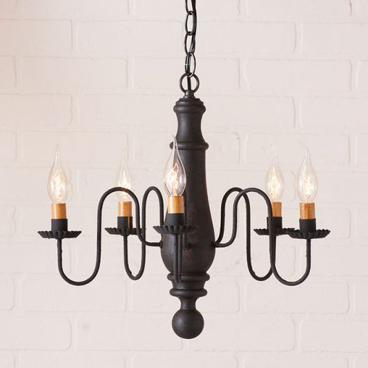 Black chandelier with five lit bulbs against a white brick wall background
