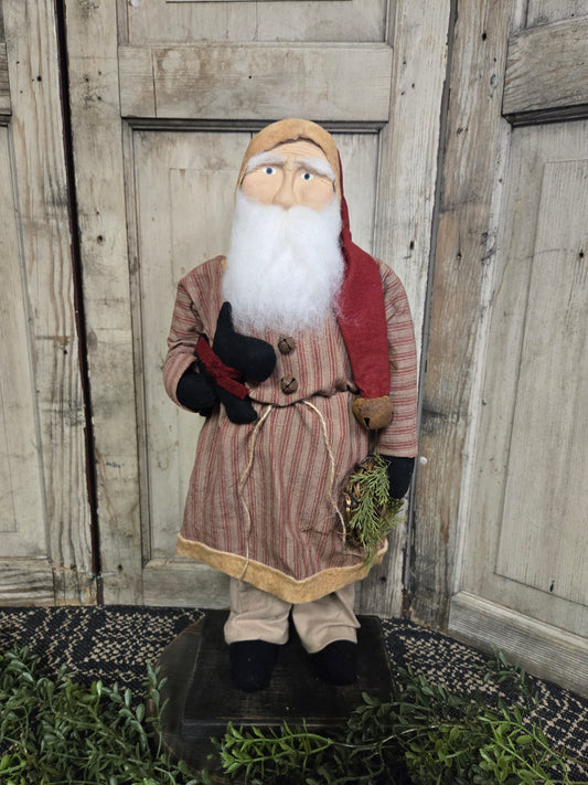 A medium-sized, primitive-style Santa figurine wearing a red and black striped coat and black hat, holding a dog on a leash. The figurine is standing against a wooden backdrop.