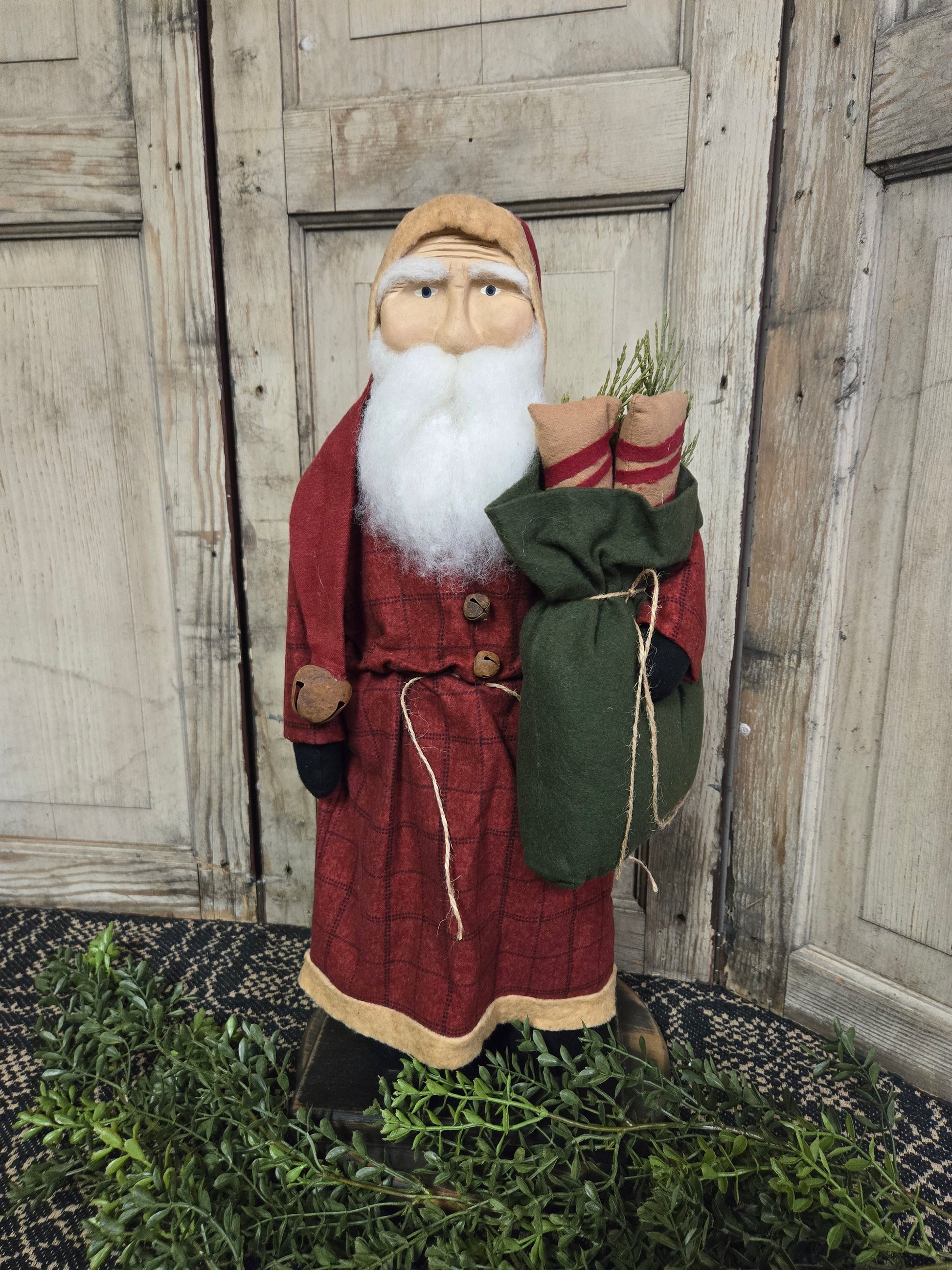 Clay faced Santa in red plaid coat holding a green sack standing against a worn wooden background
