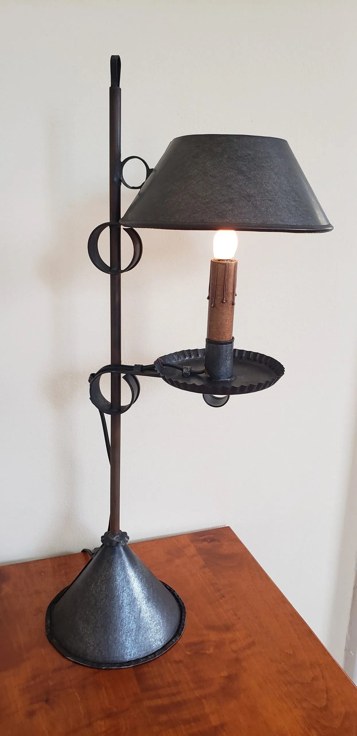 Tin light with shade on wood table in front of a cream colored wall.