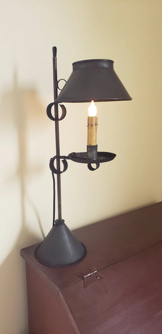 A black Meriden Tin Table Light with a lit candle inside, placed on a table with a shadow falling on the wall.
