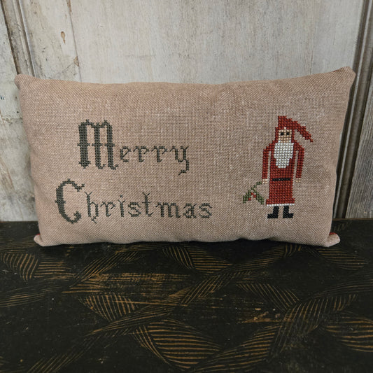 Decorative pillow with embroidered text and santa design on a wooden surface