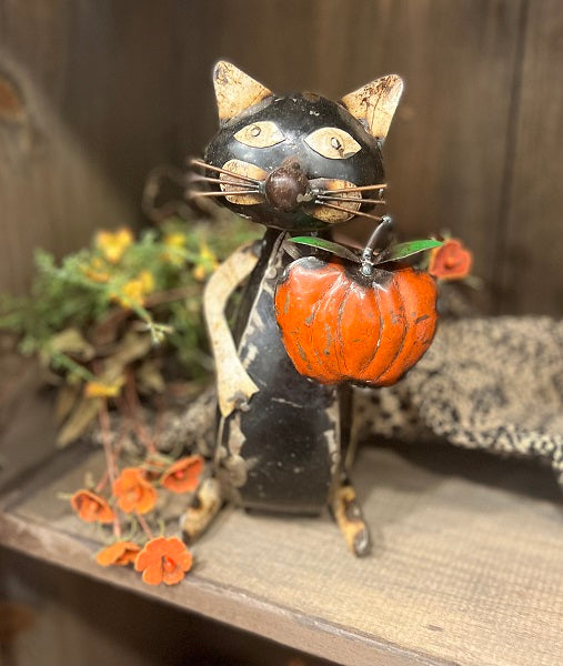 Decorative cat figurine with a pumpkin on a shelf with autumn decorations.
