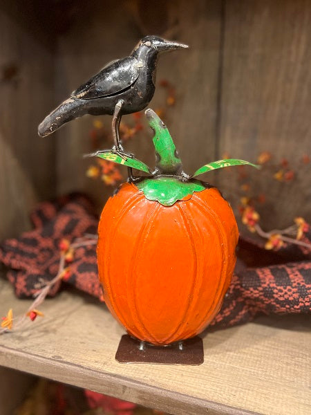 Decorative pumpkin with a crow on top, placed on a wooden surface.