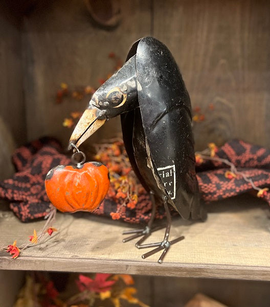 Decorative black bird with a pumpkin on a wooden surface with Halloween-themed decorations.