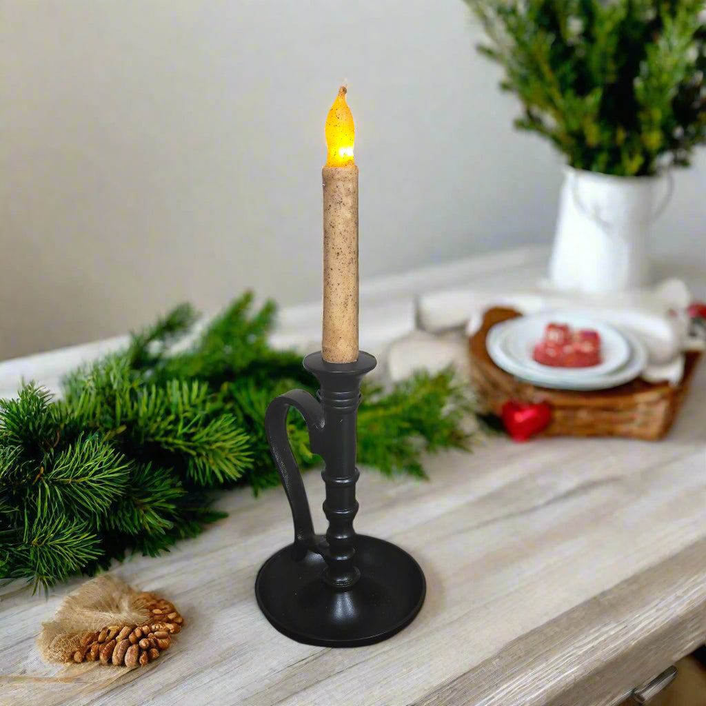 Black candle holder with a lit candle on a table with decorative items