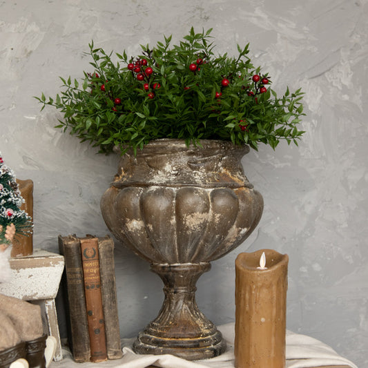 Floral pick with red berries in antique urn with candle and old books around it