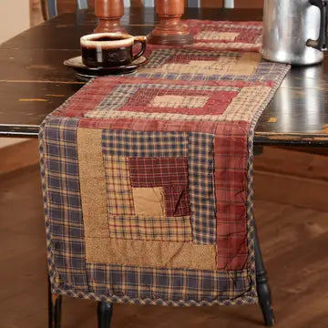 A rustic quilted table runner with a patchwork design in red, beige, and blue plaid, draped over a dark wooden dining table.