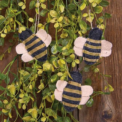 Three striped bee ornaments hanging among green leaves on a wooden background