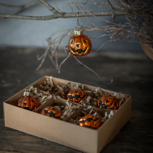 Halloween-themed decorations including jack-o'-lantern ornaments in a box with a branch in the background.