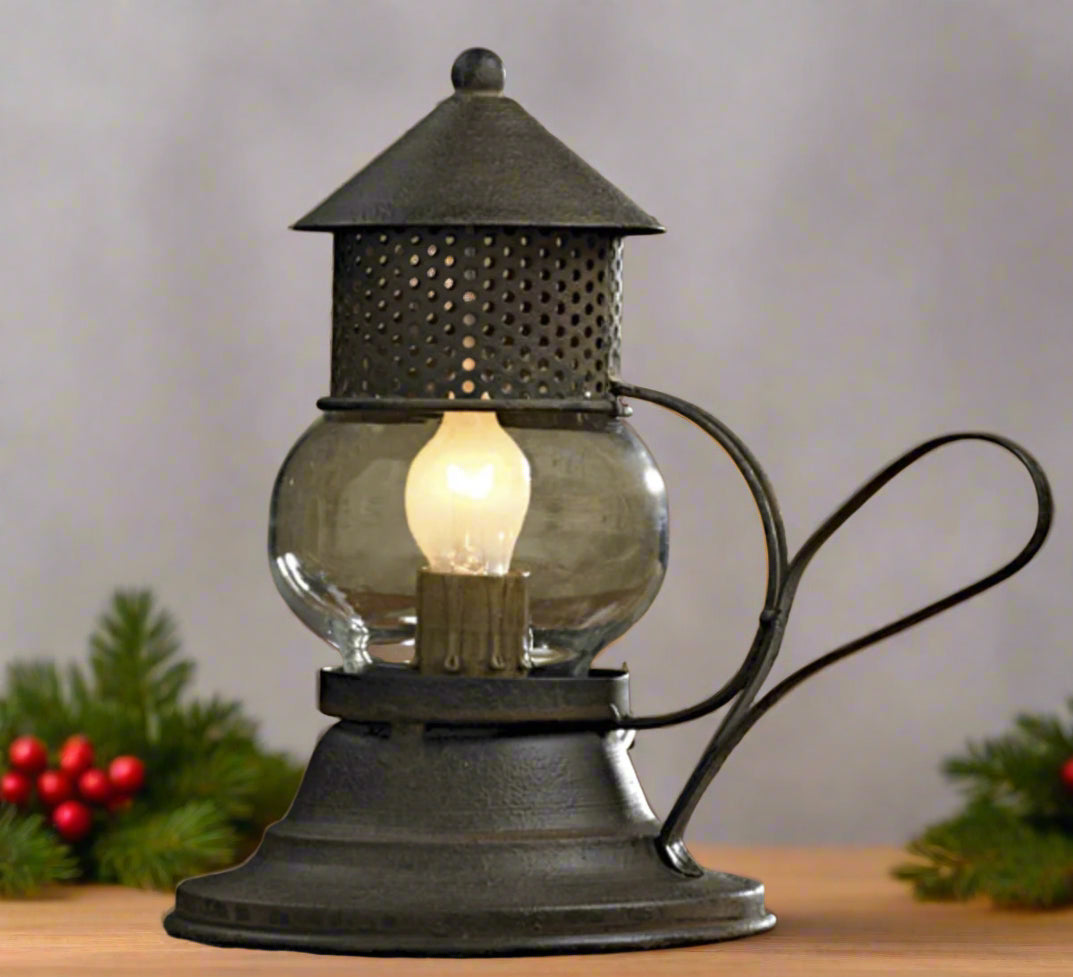 A small, vintage-style metal and glass Onion lamp with a glowing bulb, on a table surrounded by greenery