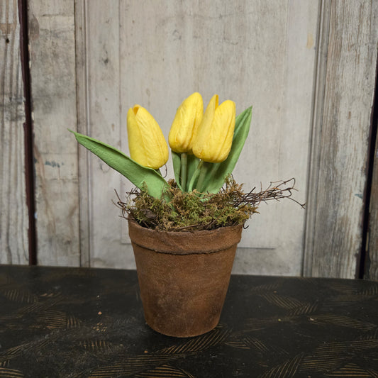 Three yellow tulips in a rustic brown pot against a wooden background