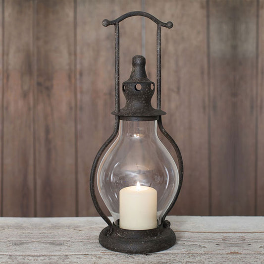 A black mini steeple lantern with a glass chimney and a lit candle inside, placed on a wooden surface.