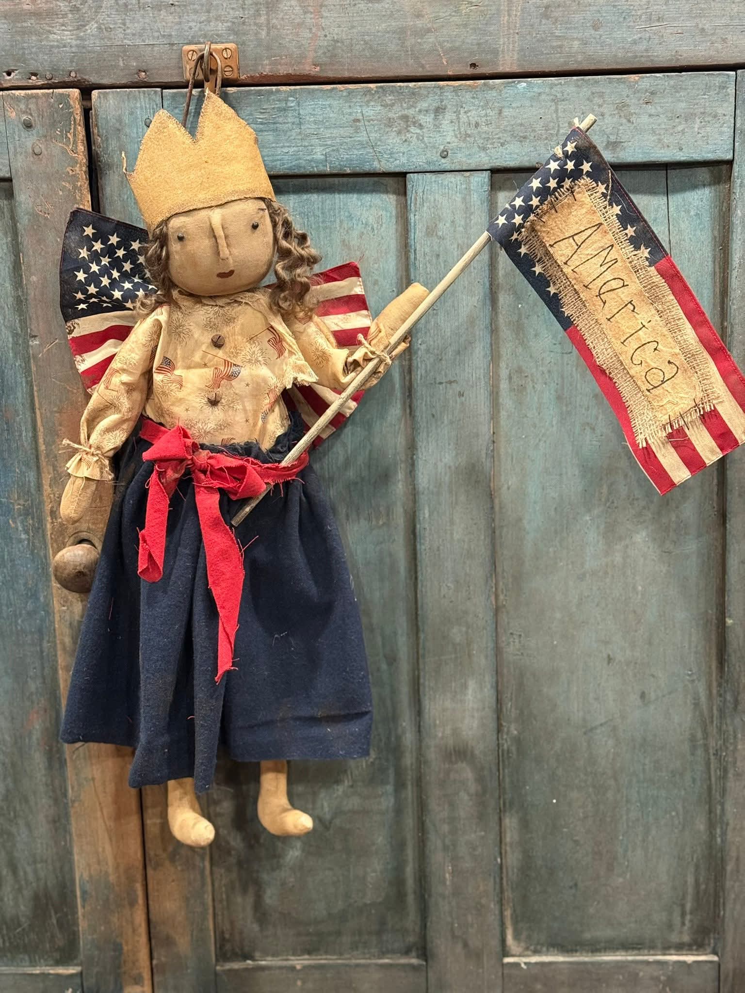 Vintage-style doll with American flag and 'America' banner against a wooden background
