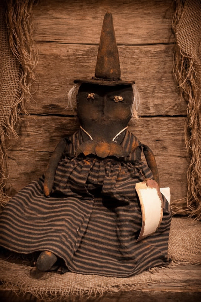 A rustic Halloween-style doll or decorative figure wearing a pointed hat and a dark striped dress, posed against a weathered wood plank backdrop with burlap and twine decorations. The text 'Primitive Kreations Wholesale' appears at the top.