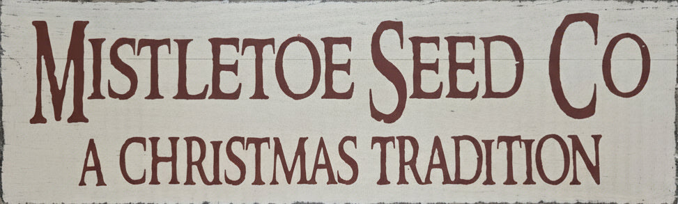 Decorative sign with 'Mistletoe Seed Co' and 'A Christmas Tradition' text on a wooden background.