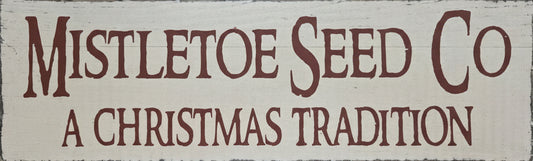 Decorative sign with 'Mistletoe Seed Co' and 'A Christmas Tradition' text on a wooden background.