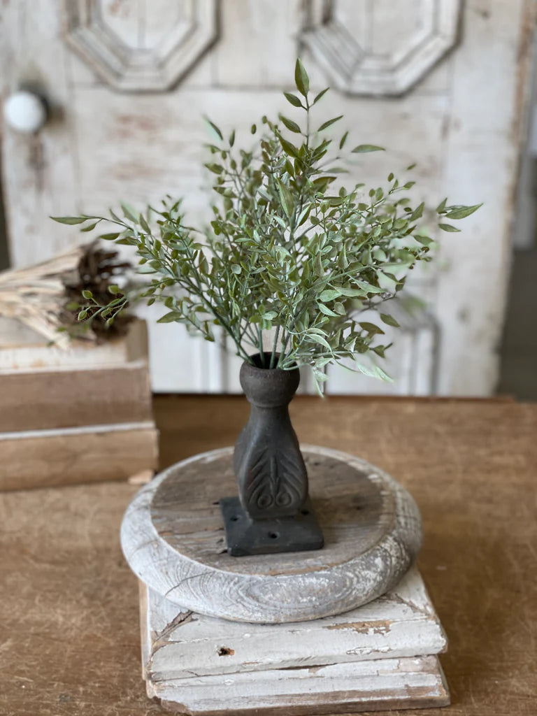 Decorative plant in a dark vase on a wooden pedestal with a rustic background