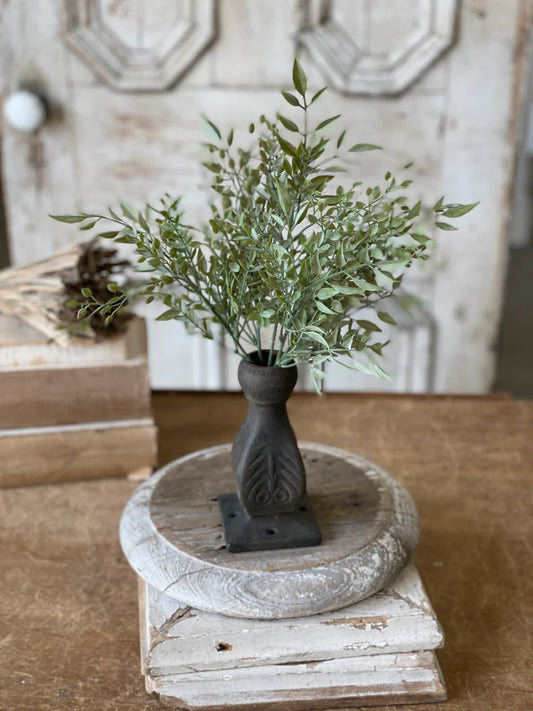 Decorative plant in a dark vase on a wooden pedestal with a rustic background