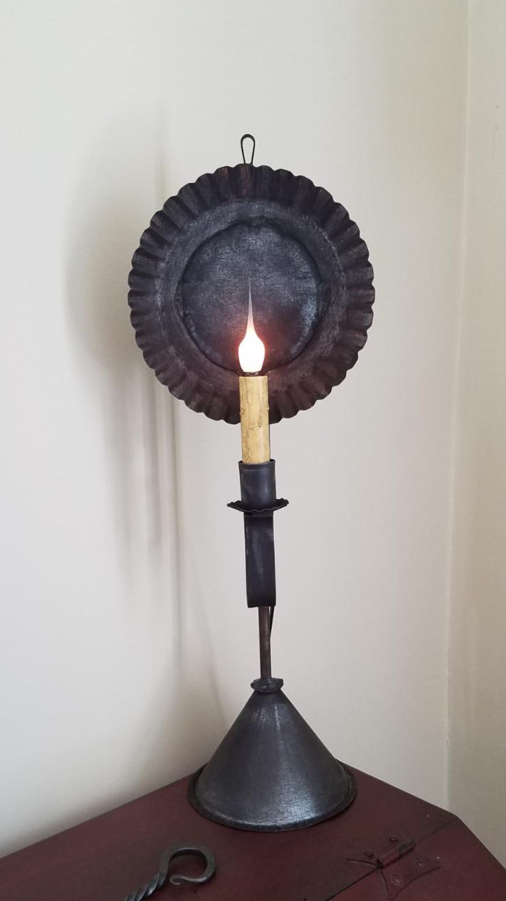 A black metal table lamp with a round shade, resembling a candle holder, on a flat base.