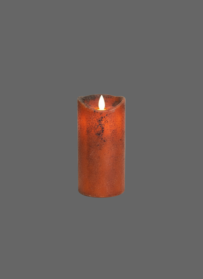 Pumpkin colored pillar candle on black riser with greenery in front of weathered wood