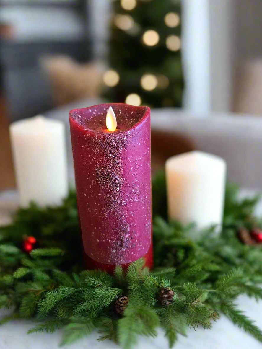 A red pillar candle with a moving flame effect on a wooden surface, with a timer switch and color speckles throughout.