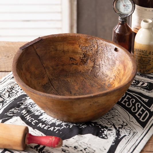 A brown resin bowl with a wooden texture, displayed on a table with a black and white checkered cloth, alongside a glass bottle and a wooden spoon.