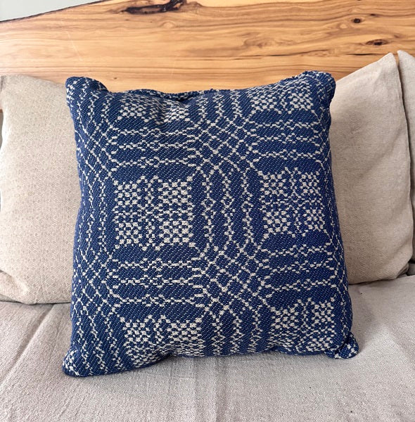 Blue patterned pillow on a gray couch with a wooden headboard.