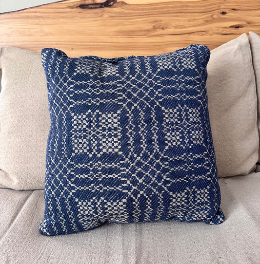 Blue patterned pillow on a gray couch with a wooden headboard.