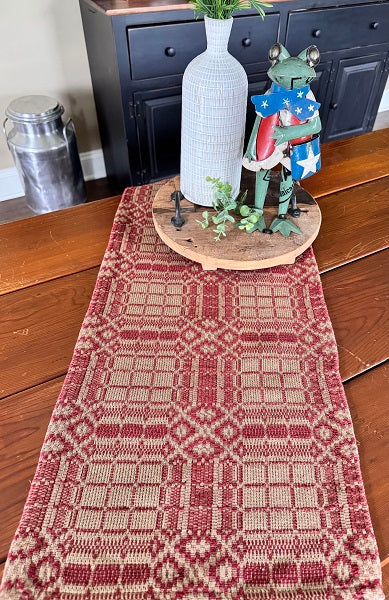 Decorative table setting with a patterned red and beige runner, a white vase, and a figurine on a wooden surface.