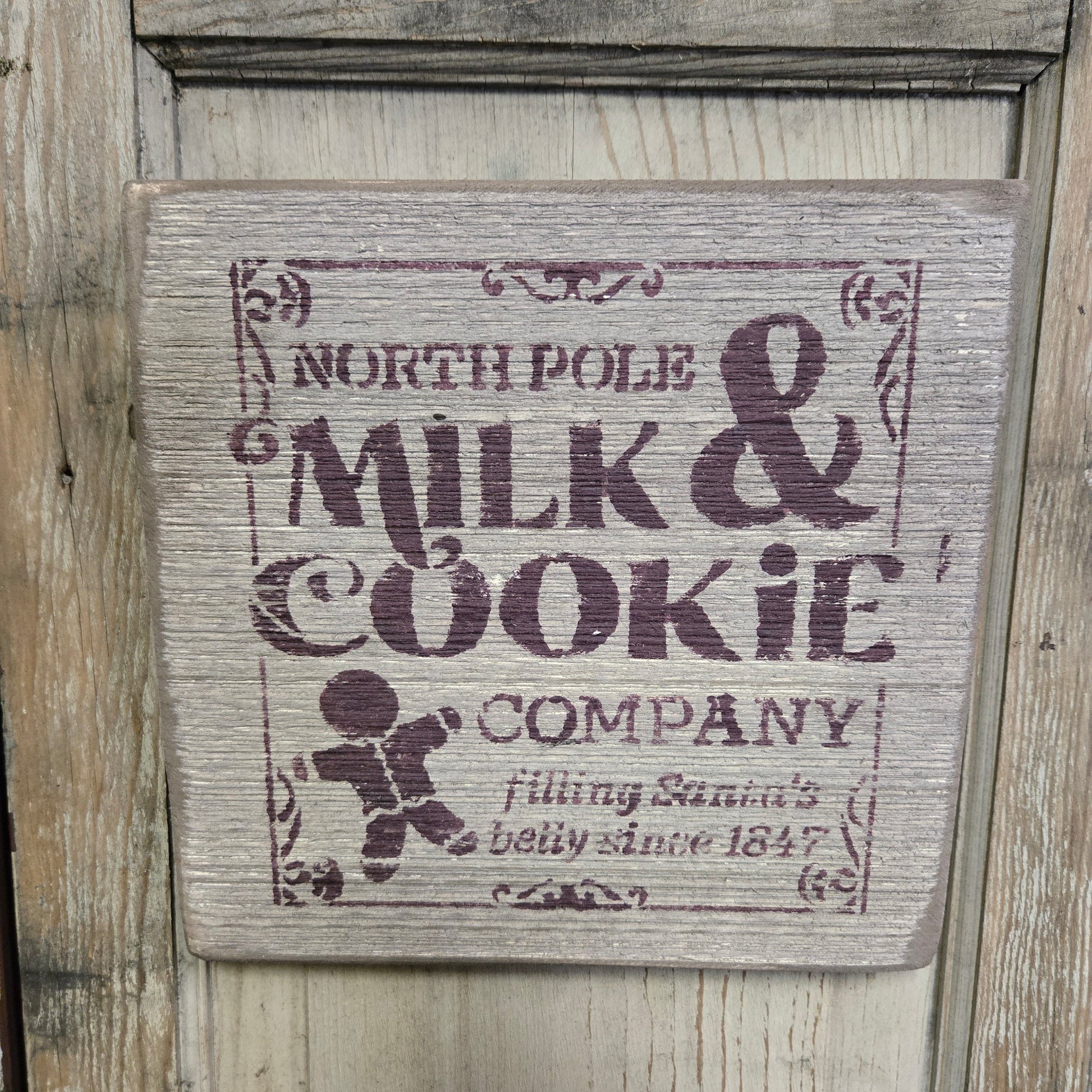 A wooden sign with a vintage design featuring the text 'NORTH POLE MILK & COOKIE COMPANY' and an illustration of a cookie.