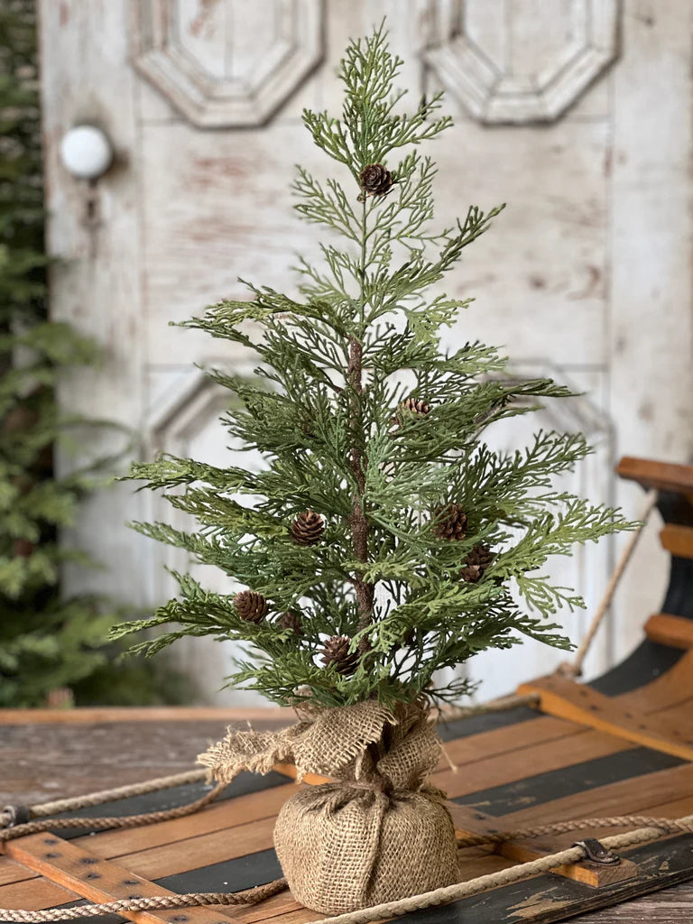 Small artificial Christmas tree with pinecones on a rustic wooden table.