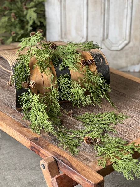 Decorative wreath with greenery and pinecones on a wooden surface