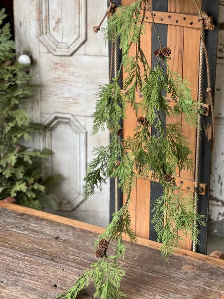 Greenery garland with pinecones hanging against a rustic wooden door.