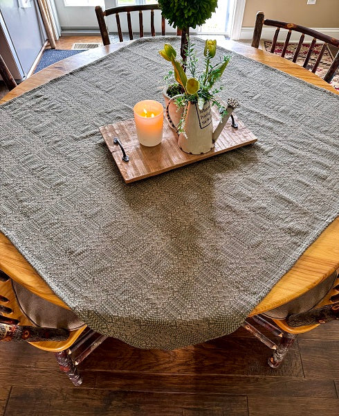 Gray textured tablecloth on a wooden dining table with a candle and floral arrangement.