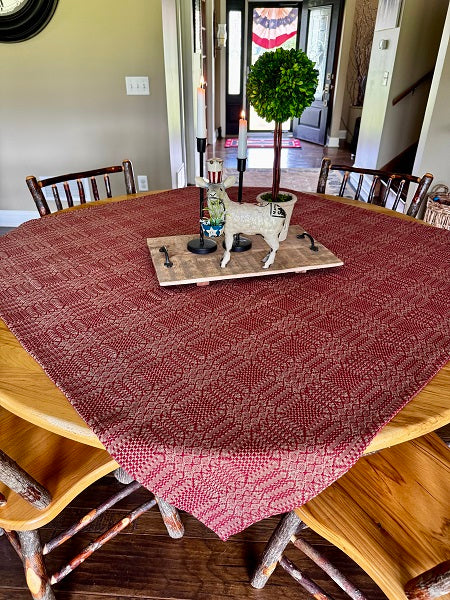 Dining room with a wooden table covered by a red patterned tablecloth, surrounded by chairs.