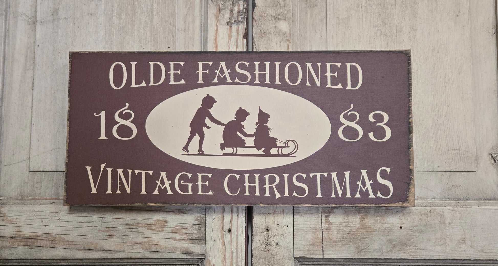 Vintage-style Christmas sign with silhouettes of children and text on a wooden background