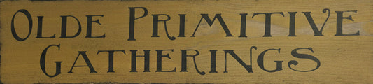 A rustic rectangular wooden sign with the words 'OLDE PRIMITIVE GATHERINGS' in dark lettering.