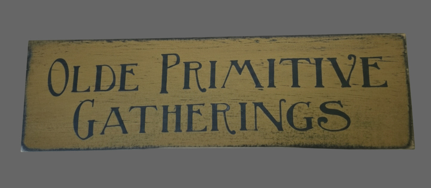 Wooden sign with 'Olde Primitive Gatherings' text on a mustard background