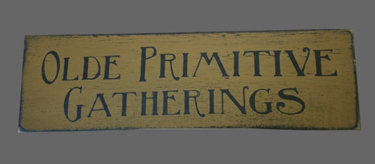Wooden sign with 'Olde Primitive Gatherings' text on a mustard background