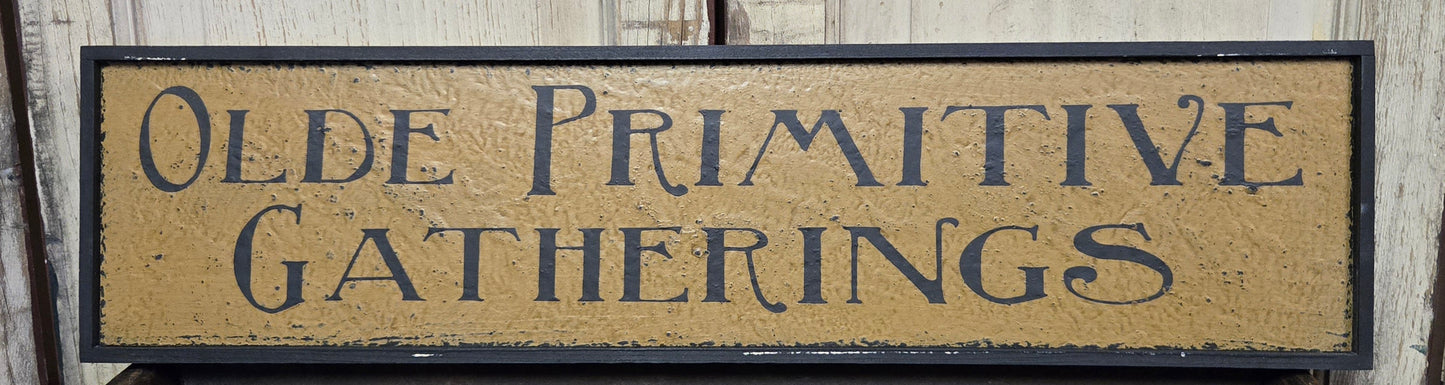 Wooden sign with 'Olde Primitive Gatherings' text on a wooden background